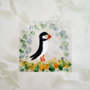 A puffin decal hand painted with a puffin and blue, green, yellow border. Photographed on a marble effect tile