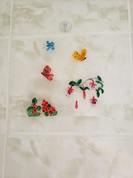 An original glass painting with 3 butterfly and fuscia flowers. Photographed on a bathroom tile